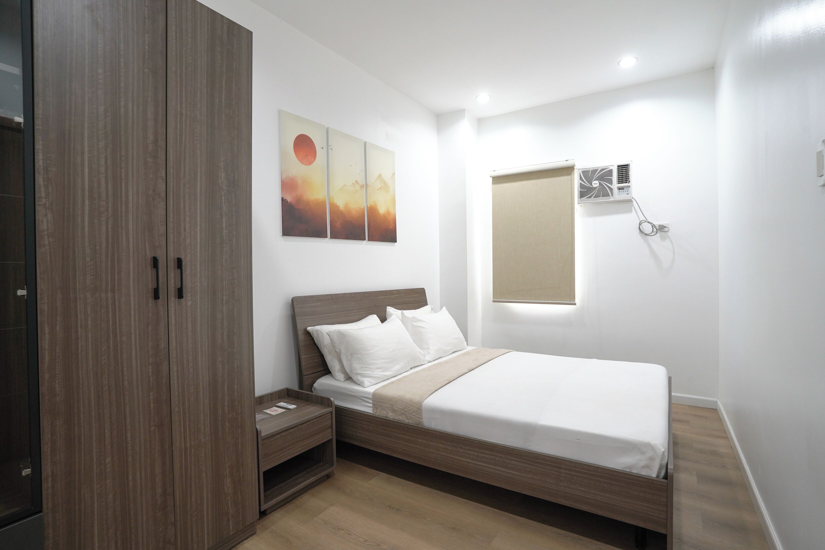 A bedroom with a bed, nightstand, wardrobe, and a wall-mounted air conditioning unit.