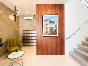 Un vestíbulo moderno con un panel de madera, un cuadro enmarcado, un sillón verde, una mesita redonda con una planta y una escalera.