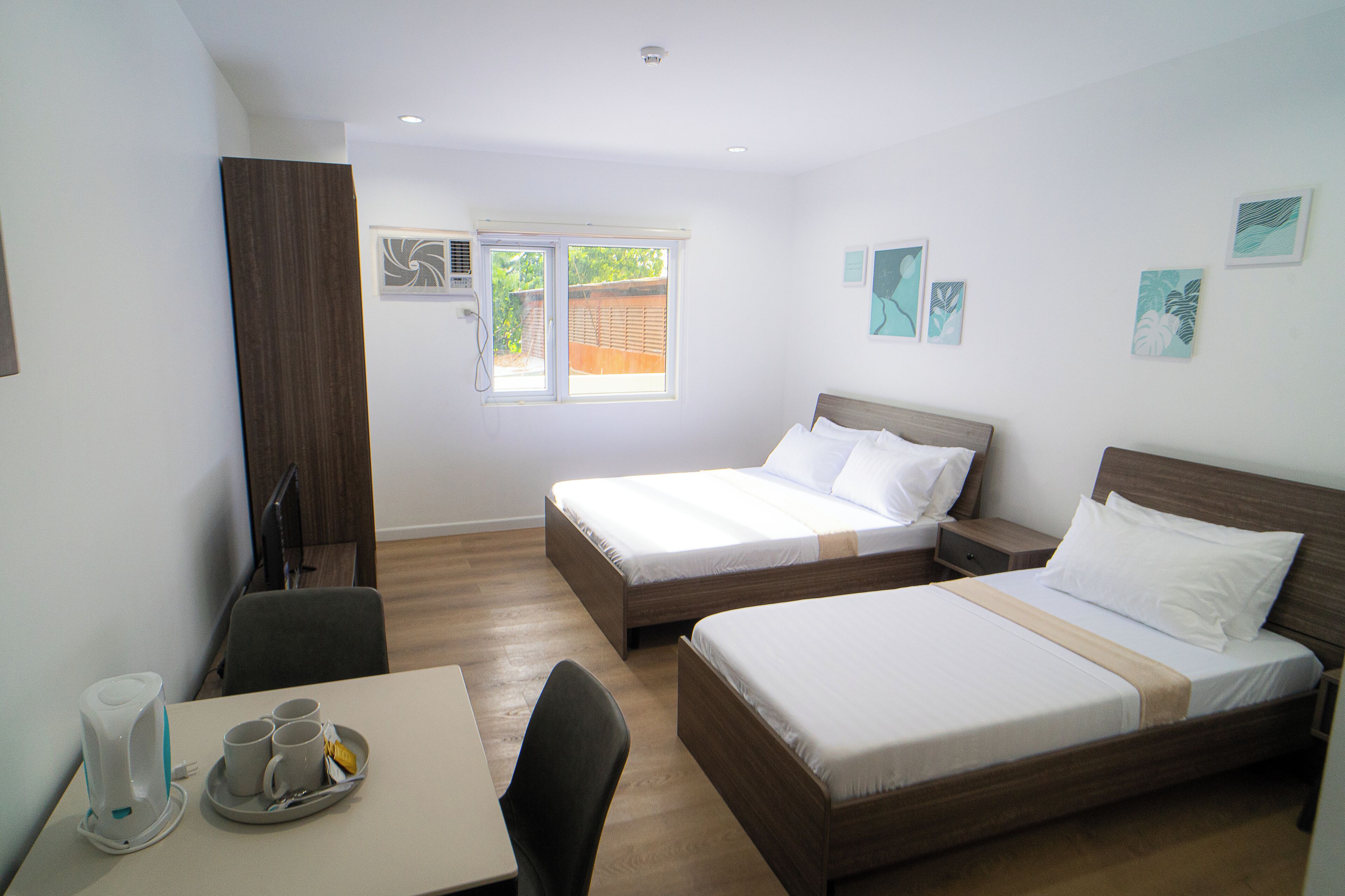A hotel room with two beds, a desk with a chair, a coffee maker, and artwork on the walls.