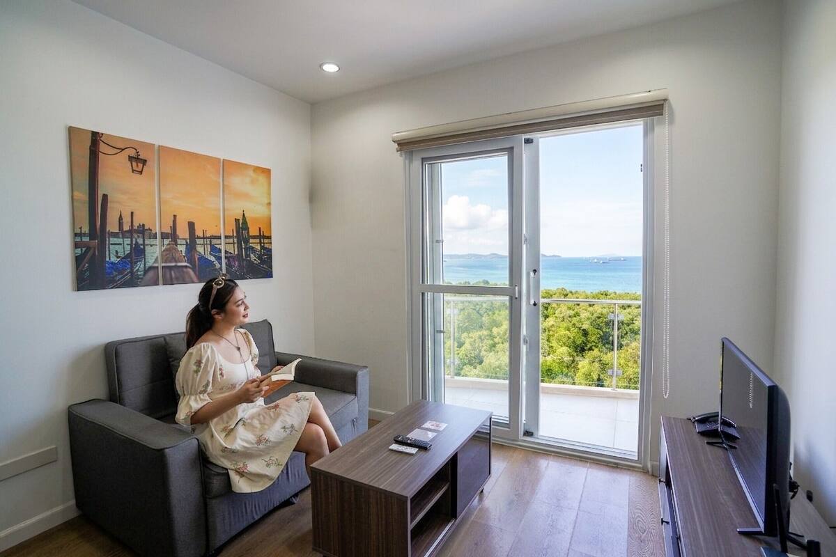 Uma sala de estar com um sofá, uma mesa de centro, uma TV e uma janela grande com vista para o mar.
