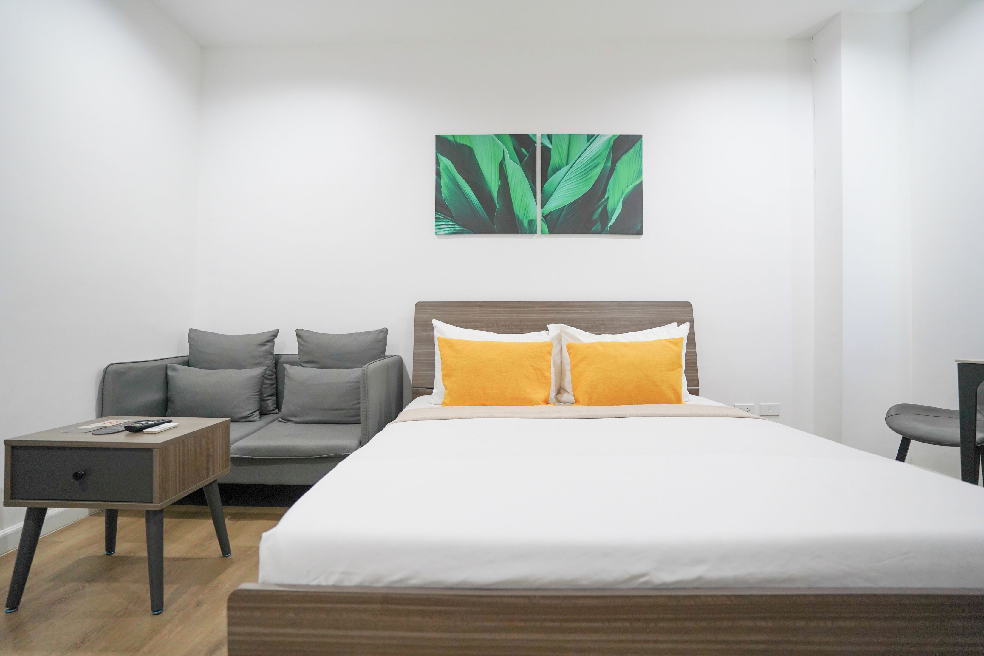 A modern hotel room with a bed, a sofa, a nightstand, and a wall-mounted artwork.