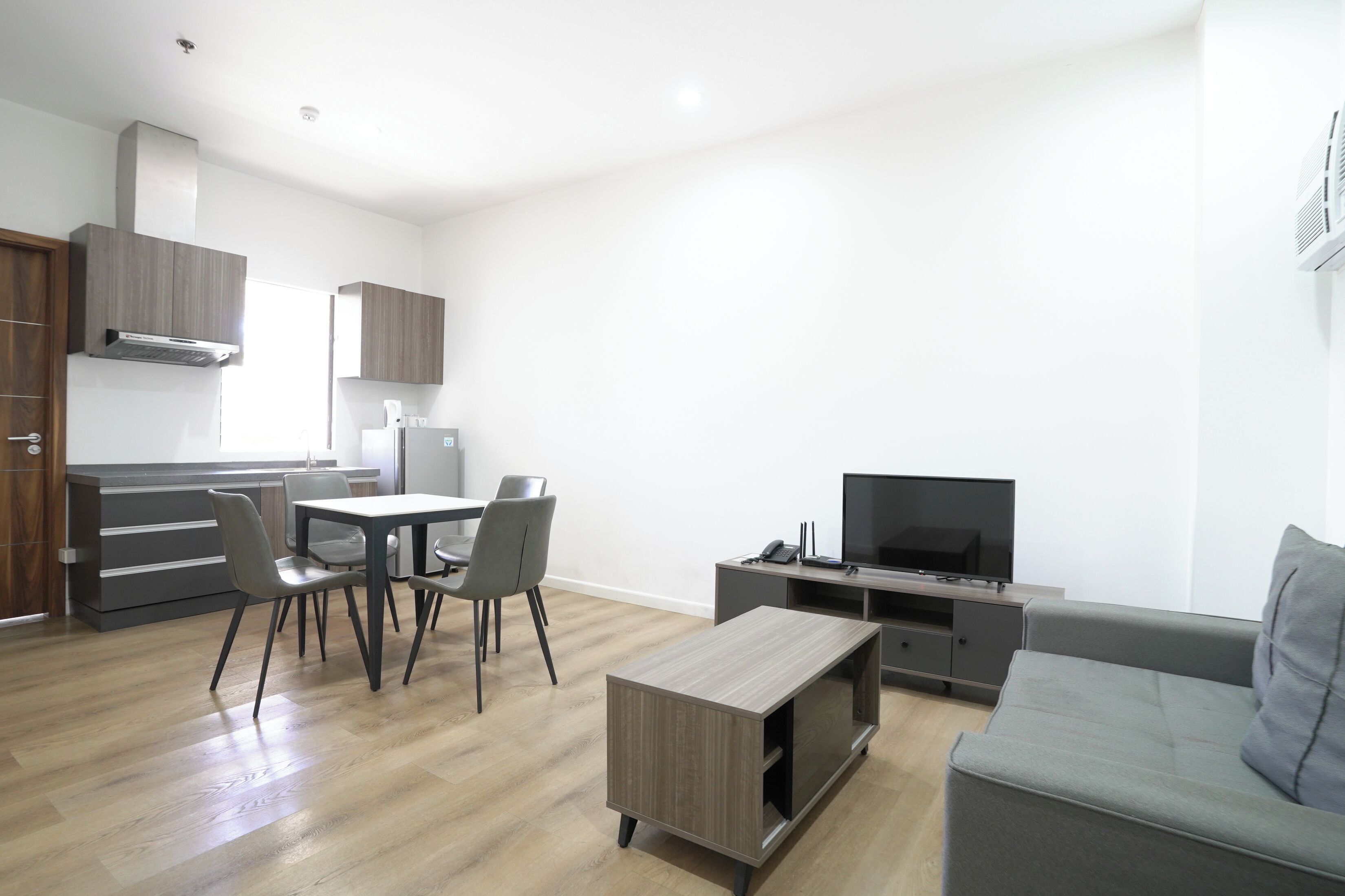 Uma sala de estar moderna com um sofá cinzento, uma mesa de centro, uma TV e um espaço de refeições com cadeiras e uma mesa.