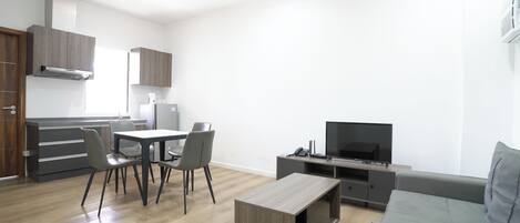 Uma sala de estar moderna com um sofá cinzento, uma mesa de centro, uma TV e um espaço de refeições com cadeiras e uma mesa.