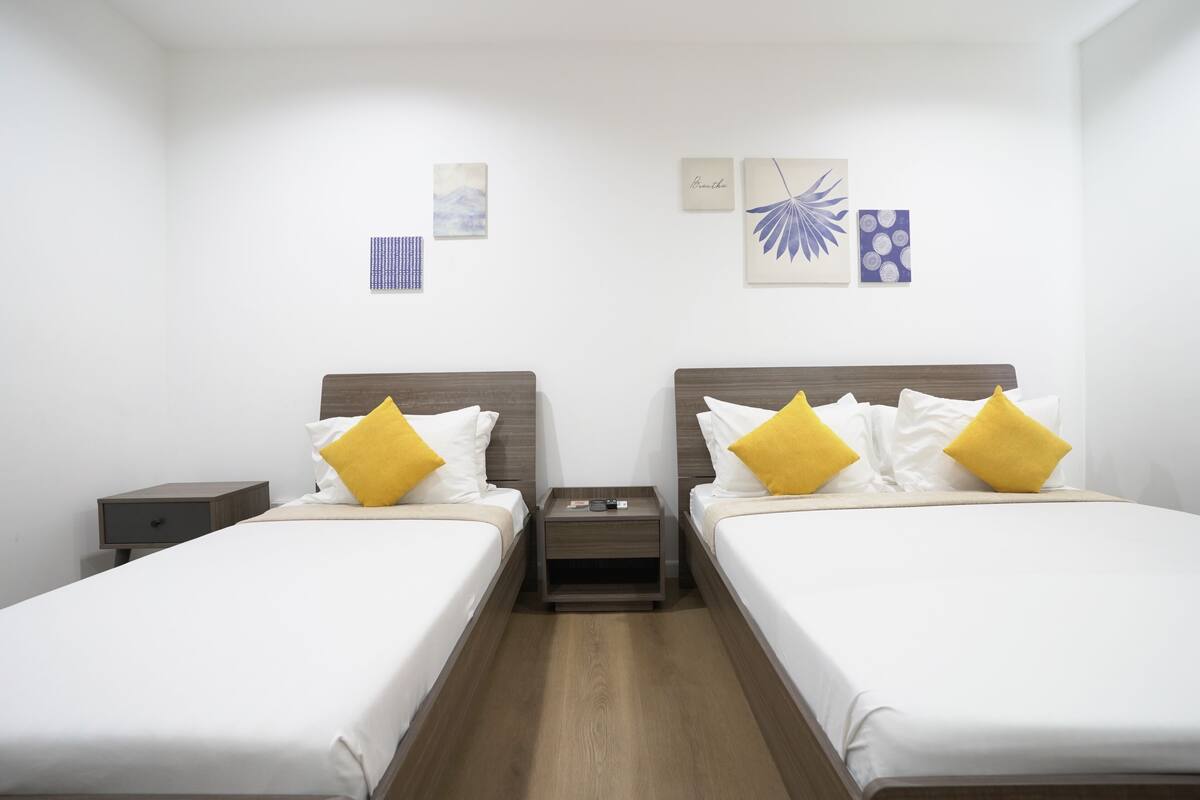 Quarto de hotel com duas camas, mesa de cabeceira, uma pequena mesa e obras de arte nas paredes.