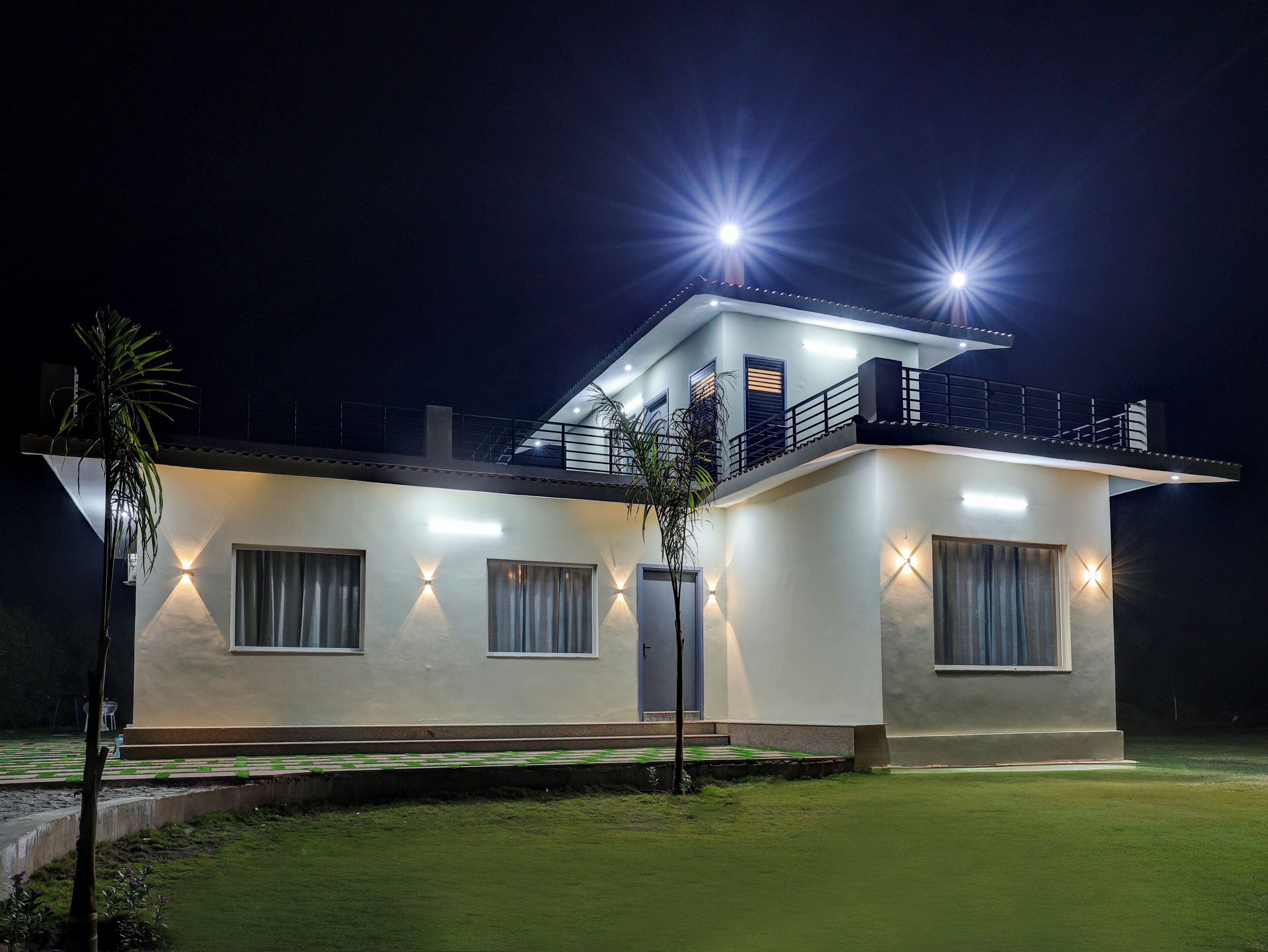 A modern two-story house with a balcony, large windows, and a well-lit exterior at night.