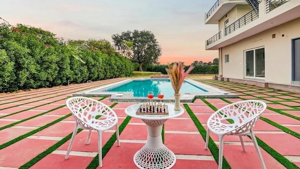 Un espace aménagé au bord de la piscine, avec une table et des chaises, une piscine et un bâtiment doté d’un balcon.