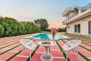 Un espace aménagé au bord de la piscine, avec une table et des chaises, une piscine et un bâtiment doté d’un balcon.
