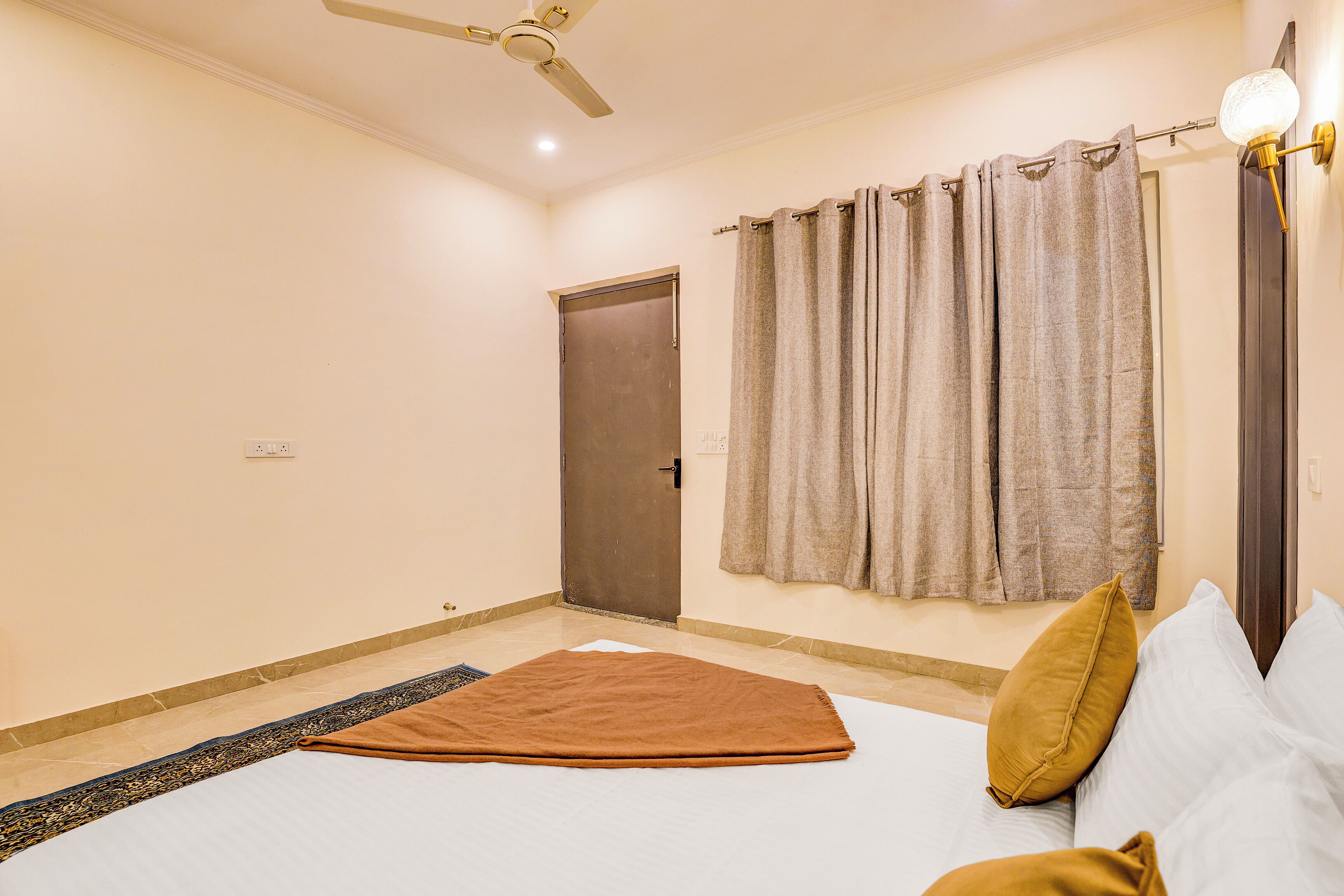 A bedroom with a bed, a ceiling fan, a door, and curtains.