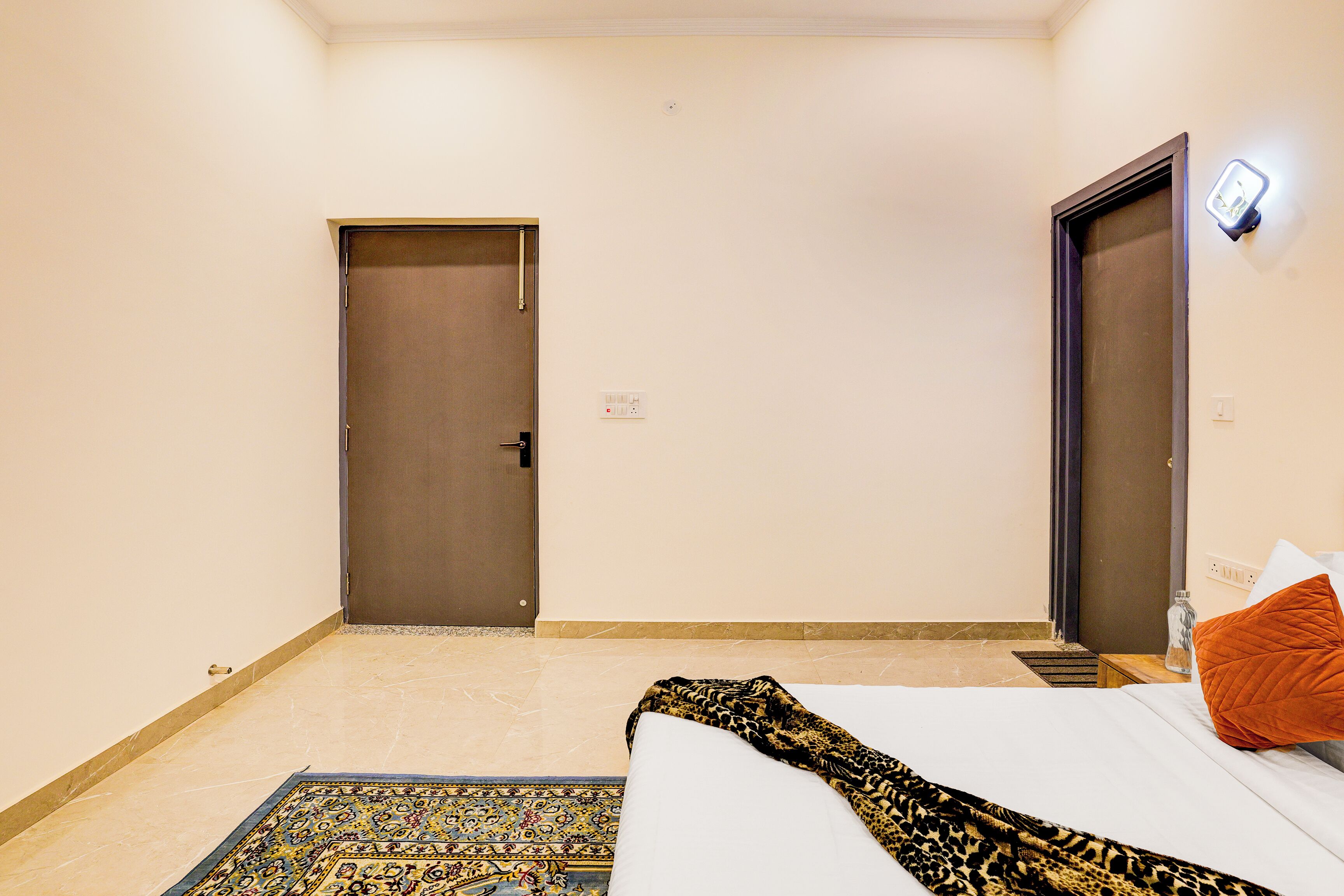 Une chambre d’hôtel avec un lit, une porte, une table de chevet et une lampe fixée au mur.