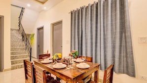 Un coin repas avec une table en bois dressée pour quatre personnes, un escalier et un rideau gris.