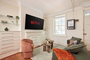 A living room with a flat-screen TV, a sofa, a chair, a small table, and a fireplace.