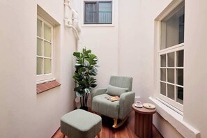 A small, cozy room with a rocking chair, a side table with a cup and saucer, a potted plant, and a window with a view.