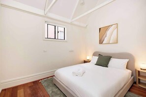 A bedroom with a bed, a window, a painting, and a nightstand with a lamp. - 4BR Surry Hills Home | Pet Friendly + Parking (Surry Hills)