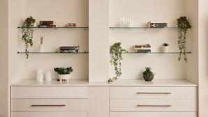 Et minimalistisk rum med to hvide skabe, en hvid bordplade og glashylder med bøger, planter og pyngeting.