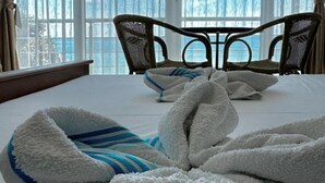 A hotel room with a bed, two chairs, and a view of the sea through large windows. - Casa Mila Apartments & Bungalows (Utjeha)