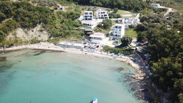 An aerial view of a coastal area with a small boat in the water, surrounded by buildings and greenery. - Casa Mila Apartments & Bungalows (Utjeha)