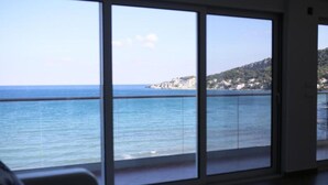 A room with large windows offering a view of the sea and a hilly landscape. - Casa Mila Apartments & Bungalows (Utjeha)