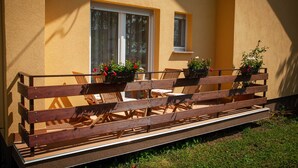 An outdoor seating area with wooden benches and tables, potted plants, and a window. - Apartments Slavek (Jastrebarsko)