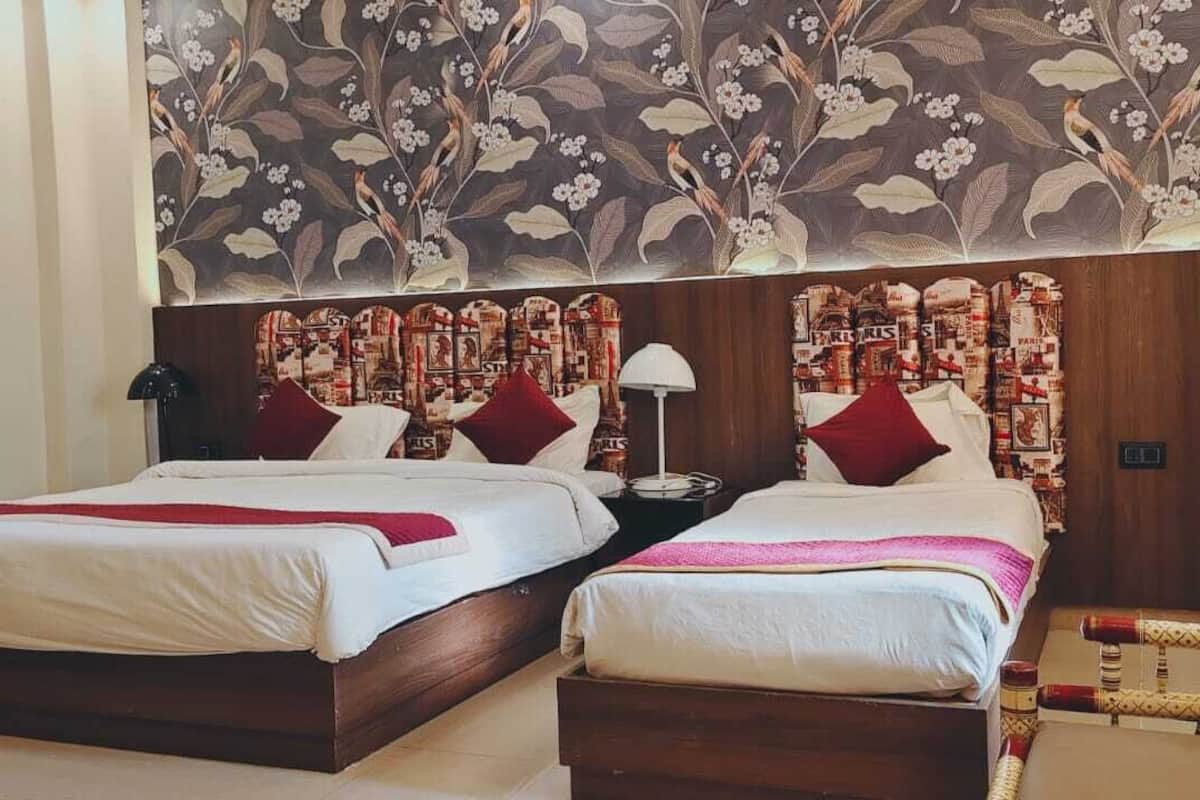A double room with two beds, a wooden headboard, a floral wall mural, and a small nightstand with a lamp.