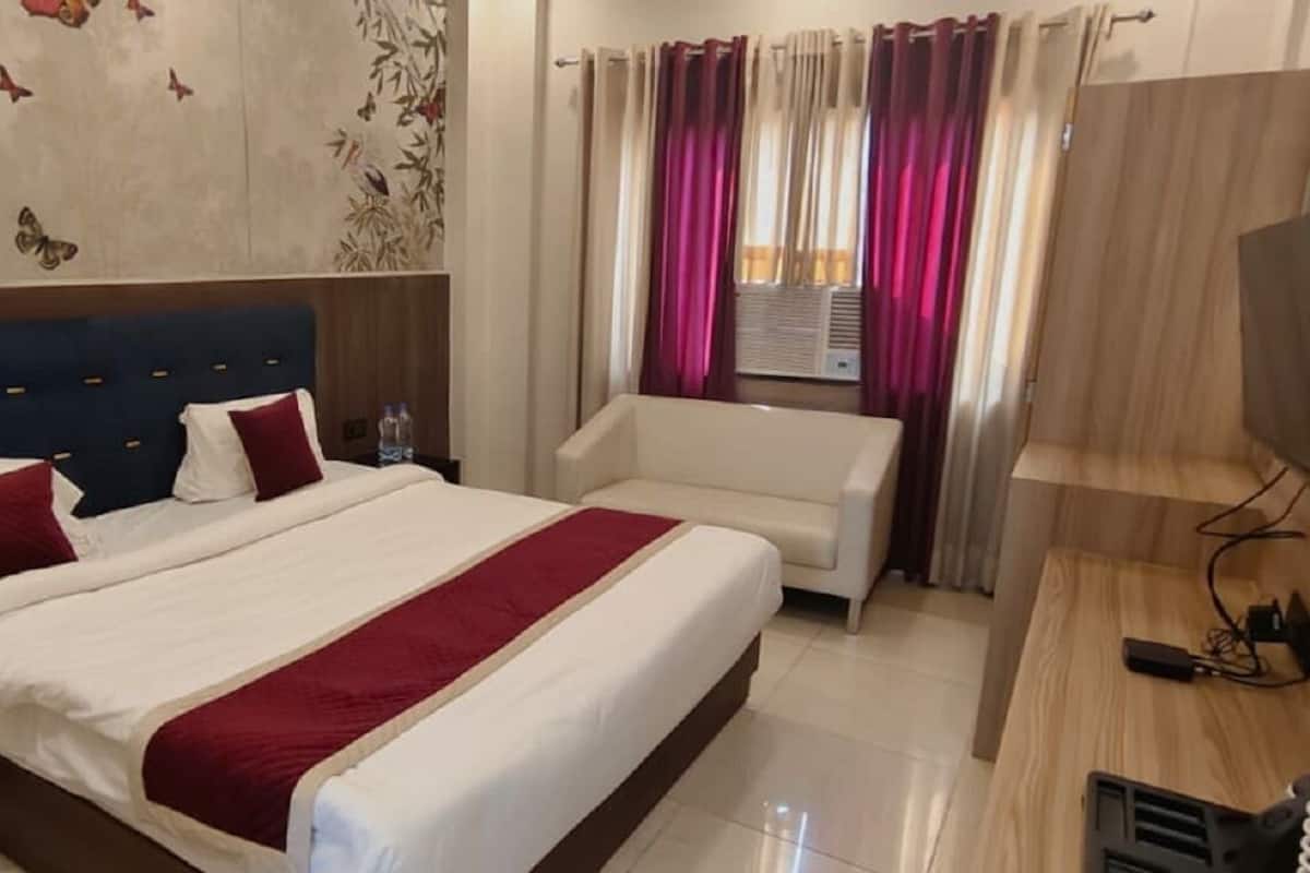 A hotel room with a large bed, a sofa, a TV, and a window with curtains.