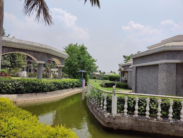 A serene courtyard with a narrow water channel, stone walls, and lush greenery. - MJ FUNCITY WATER PARK &RESORT (Bakshi Ka Talab)