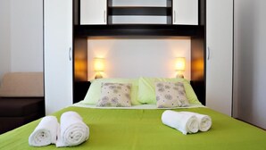 A neatly made bed with green bedding and two rolled towels, a bedside lamp, and a headboard with built-in lighting. - Apartments Nena (Kukljica)