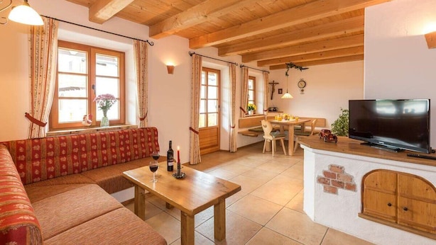 A cozy living room with a wooden ceiling, a sofa, a dining table with chairs, a TV, and a fireplace. - Vacation apartment Anastasia (Chieming)