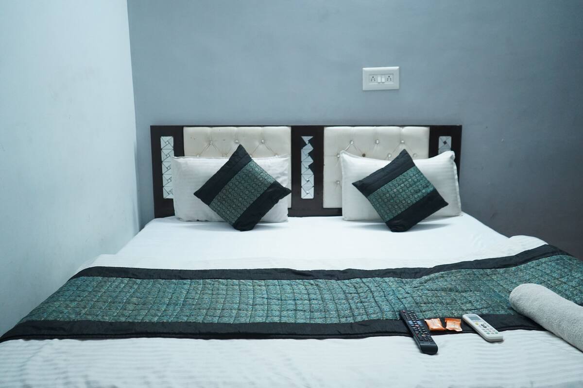 Un lit bien fait, avec une couvre-lit matelassé, deux oreillers et une télécommande posée sur le lit.