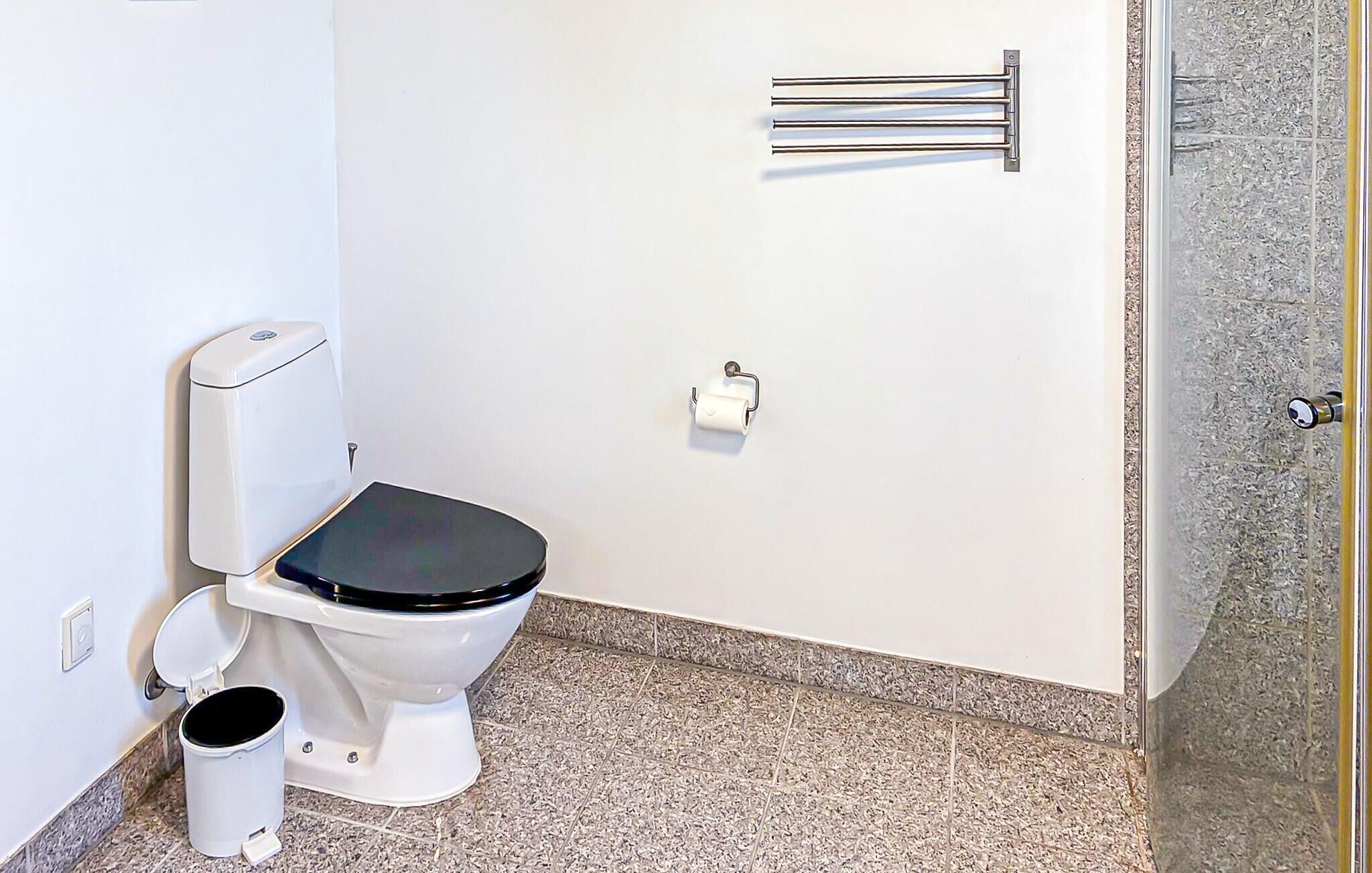 Ein Badezimmer mit Toilette, Handtrockner, Papierhandtuchspender und Duschbereich.