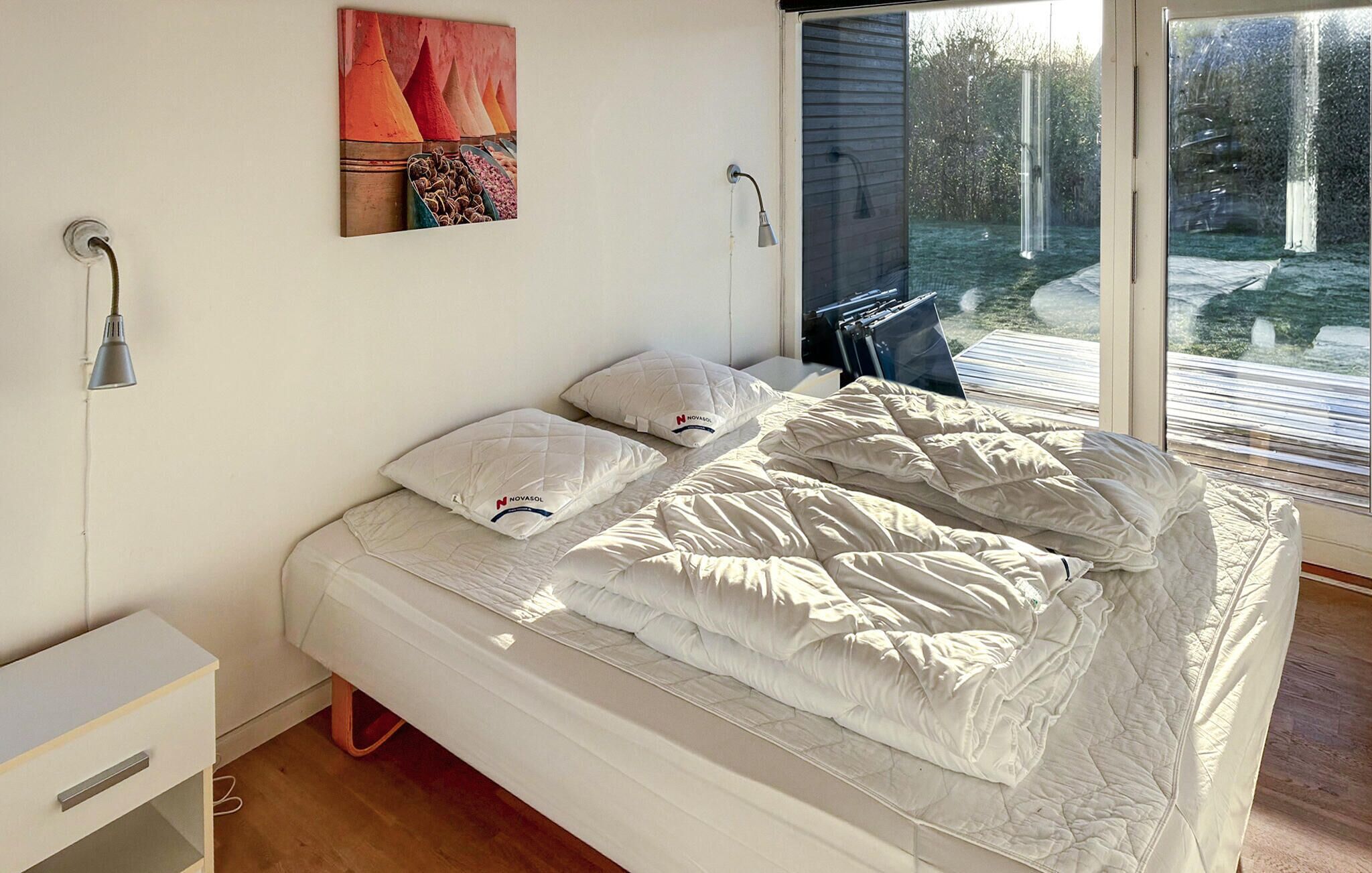 A bedroom with a bed, pillows, a bedside table, a lamp, and a window with a view of the outdoors.
