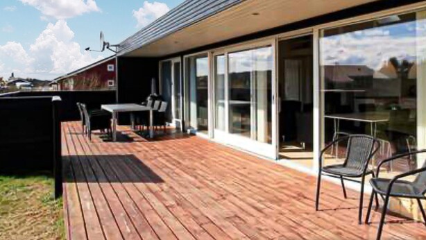 A modern building with a wooden deck, outdoor seating, and large glass doors leading to an interior space. - 3 bedroom amazing home in Brovst (Brovst)