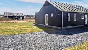 A modern building with a sloped roof, a gravel driveway, and a grassy field in the background. - 3 bedroom amazing home in Brovst (Brovst)