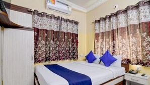 Habitación de hotel con cama, cortinas, armario, mesita de noche y aire acondicionado.