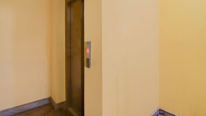 Un pasillo estrecho con suelo de madera, puerta cerrada de ascensor y panel de control de ascensor en la pared.