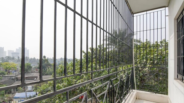 Un balcón con barandillas metálicas que da a un jardín y una vista panorámica de la ciudad.