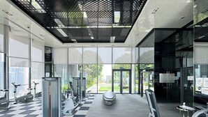Ein modernes Fitnessstudio mit Schachbrettmuster-Boden, unterschiedlicher Trainingsgeräte und großen Fenstern mit Blick ins Freie.