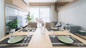 Ein zeitgemäßer Essbereich mit einem Holztisch, gedeckt für zwei Personen, einer Blumenvase und einer Couch im Hintergrund.