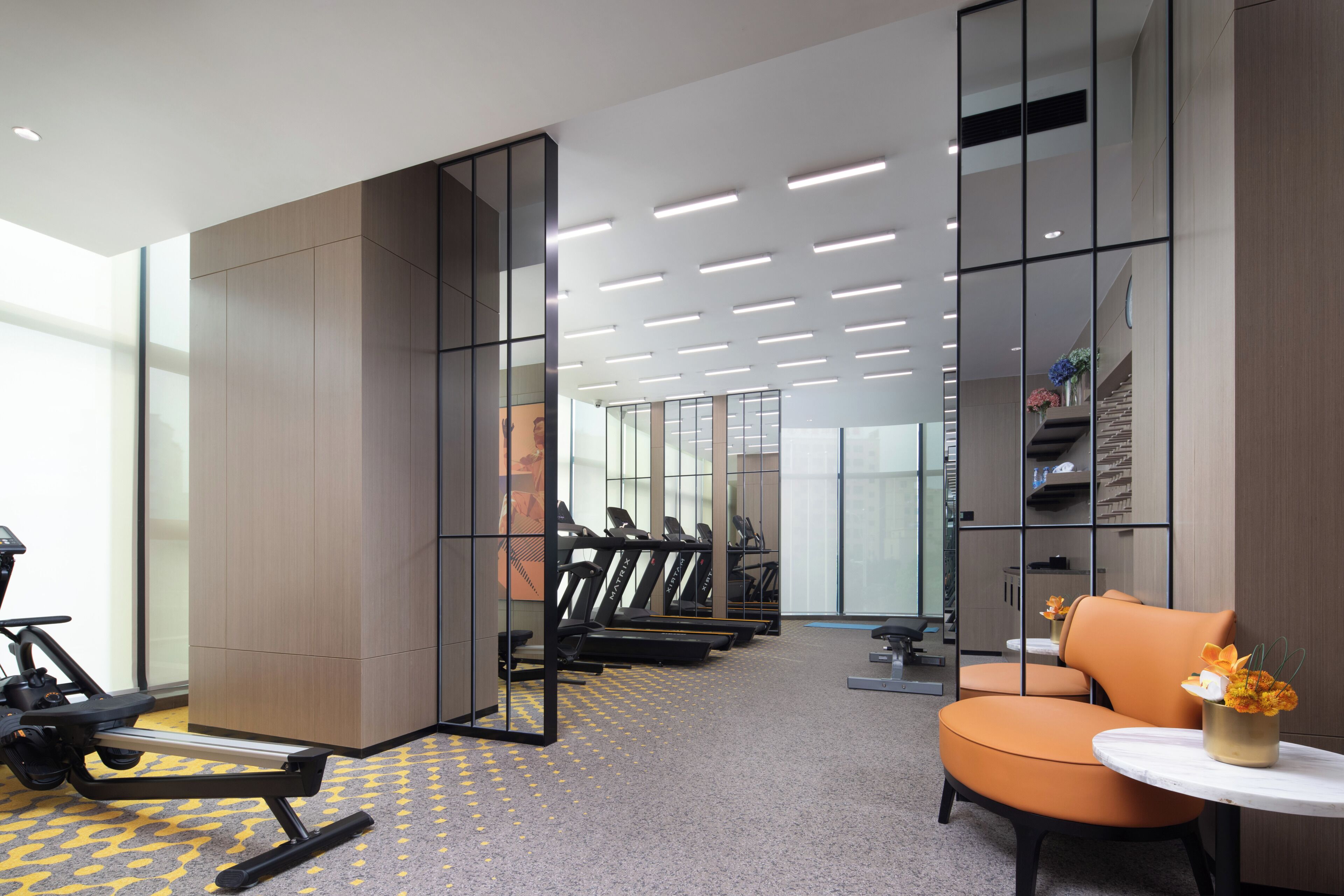 Een moderne sportschool met trainingsapparatuur, een zithoek met een bloemenvaas en een groot raam voor natuurlijk licht.