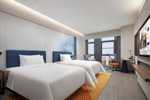 Une chambre d’hôtel avec deux lits, un bureau, une chaise, une télévision et une grande fenêtre.