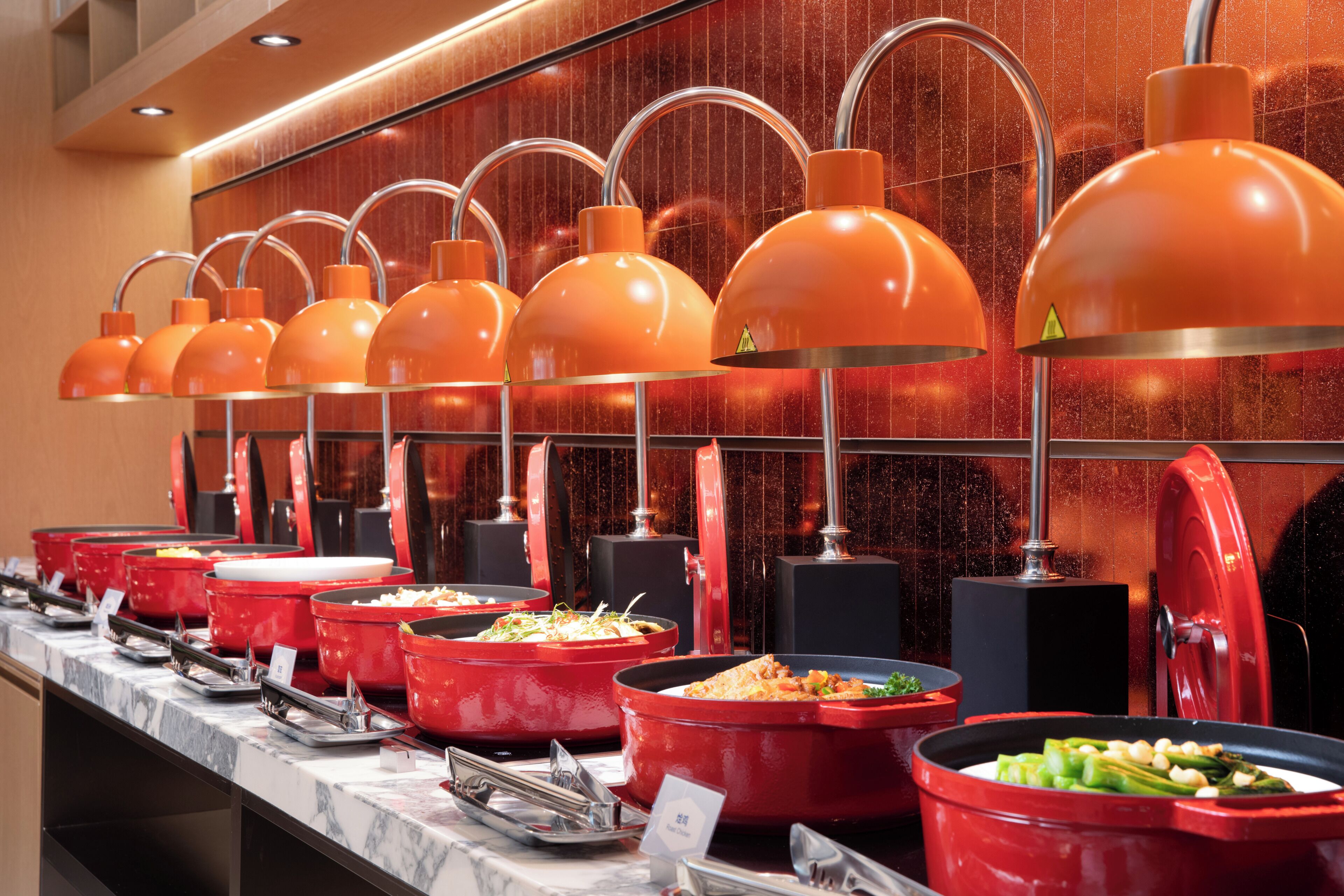 A buffet with multiple red serving stations and overhead orange lamps.