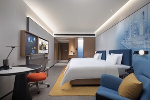 A modern hotel room with a large bed, a desk, a chair, a sofa, and a cityscape mural on the wall. - Hampton by Hilton Jinjiang Airport (Quanzhou)