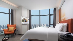 A modern hotel room with a large bed, a chair, a TV, and a city view. - Hampton by Hilton Jinjiang Airport (Quanzhou)