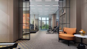 A modern office space with a treadmill, exercise equipment, and a seating area with a vase of flowers. - Hampton by Hilton Jinjiang Airport (Quanzhou)