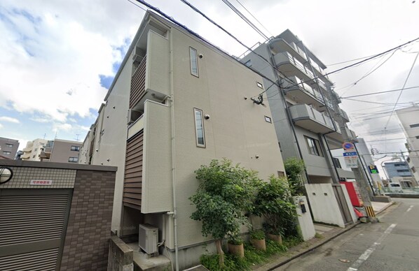 Un edificio residencial de varios pisos con fachada plana, equipos de aire acondicionado y entrada con reja.