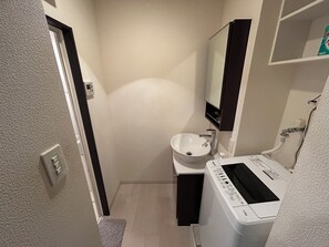 Un baño pequeño con un lavabo blanco, un espejo y una lavadora blanca.