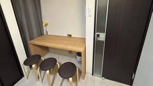 Una habitación pequeña con una mesa de madera, tres taburetes, un reloj en la pared y una puerta con un panel de vidrio esmerilado.