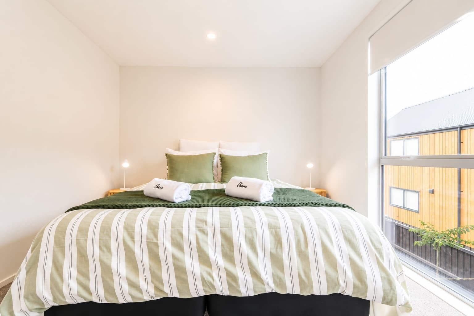 A hotel room with a bed, pillows, and a view of a building through a window.