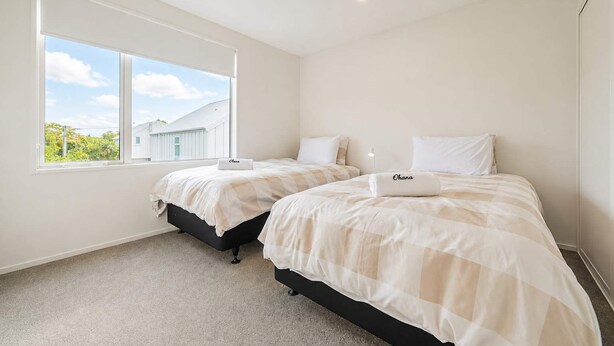 A bedroom with two beds, a large window, and a view of a house.