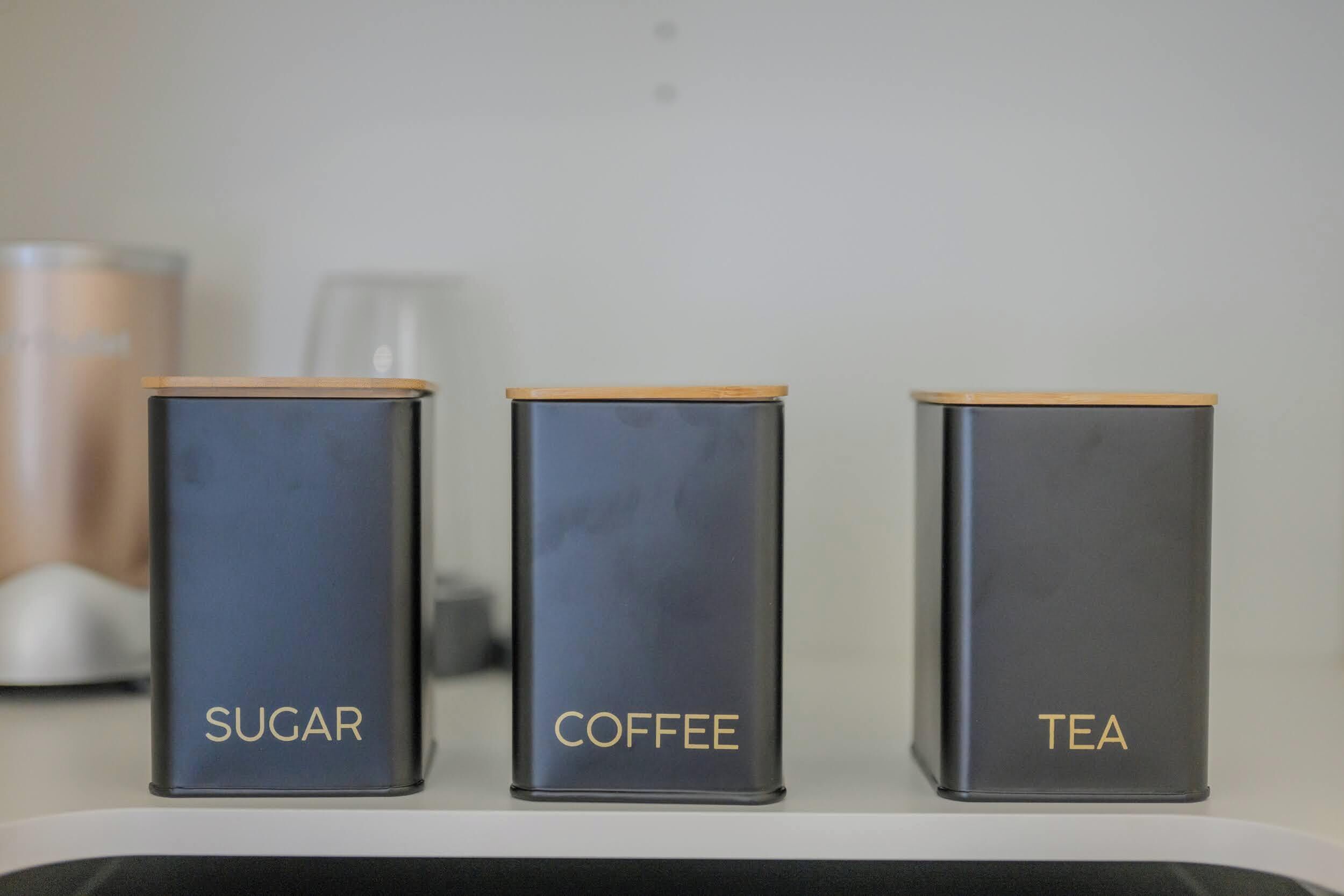 Three containers labeled 'SUGAR,' 'COFFEE,' and 'TEA' on a shelf.