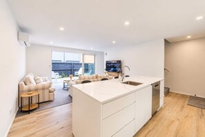 A modern kitchen with a central island, a dining area with a sofa and chairs, and a TV in the background.